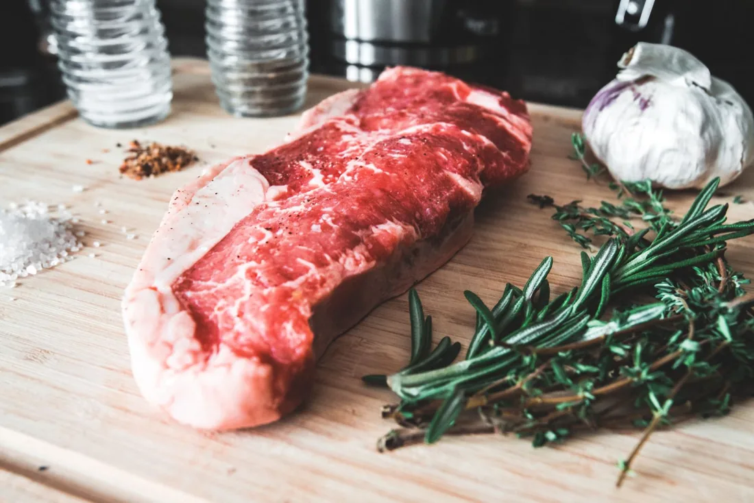 Illustrative photo of raw beef steak with garlic and herbs on a wooden board