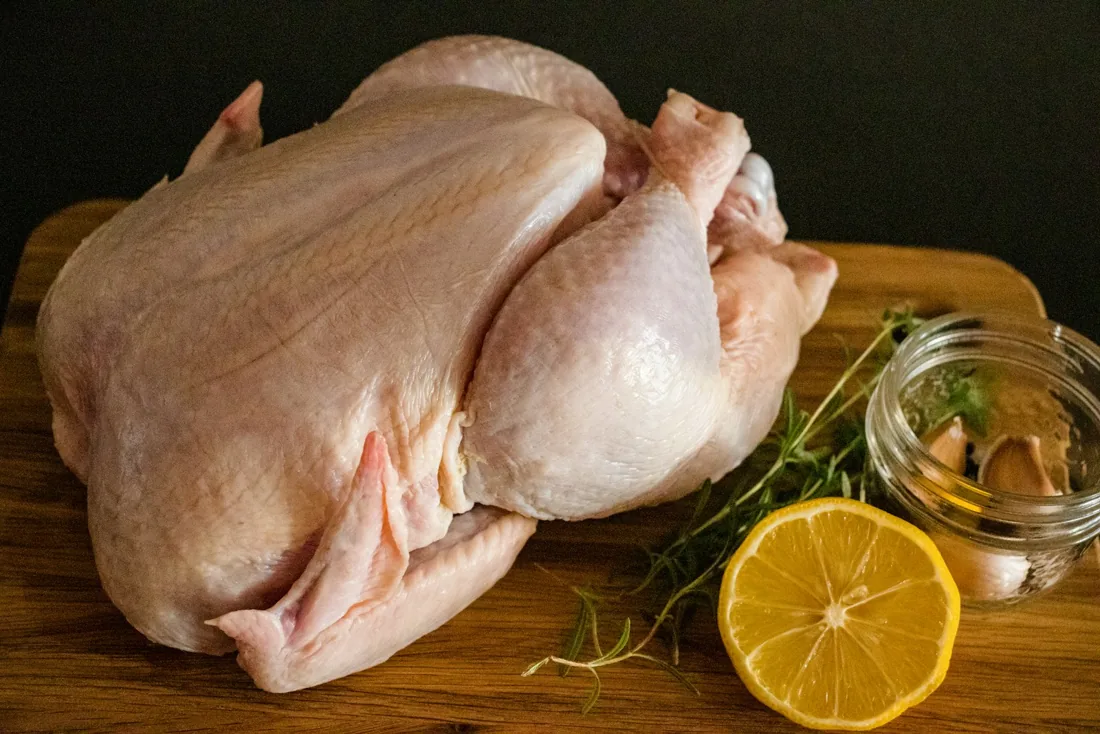 Illustrative photo of a whole raw chicken on a board with lemon and herbs
