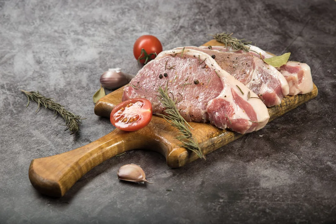 Illustrative photo of raw pork chops with tomatoes and herbs