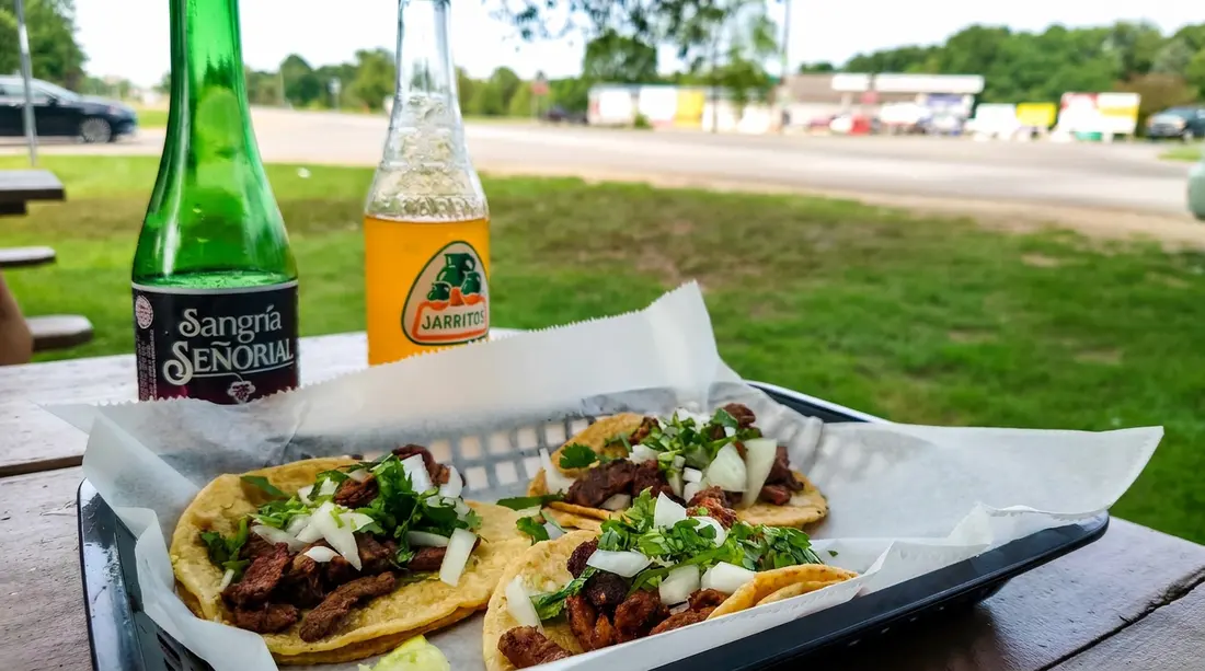 La Perla tacos topped with meat, onion, and cilantro alongside bottled drinks