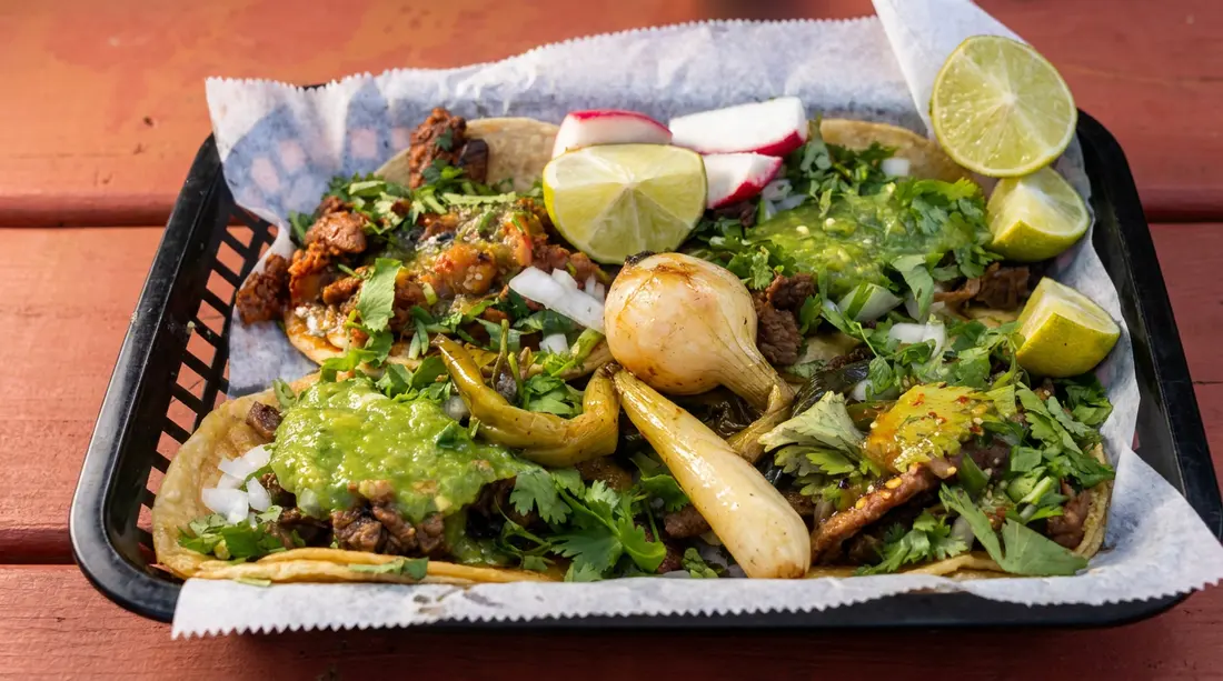 A tray of tacos with grilled meat, onion, cilantro, lime, and radish
