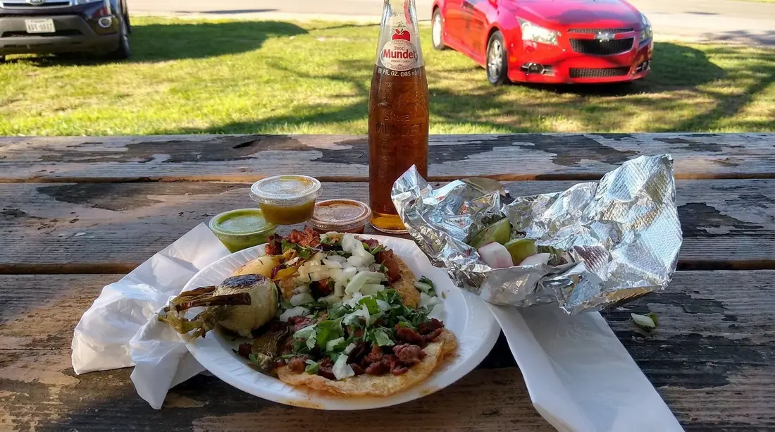A taco meal, foil wrappers, and salsa on an outdoor table